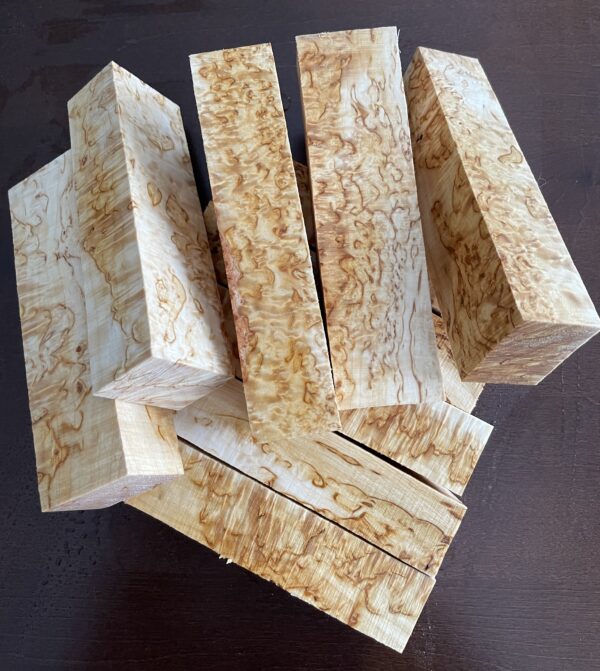 A set of ten curly birch handle blocks arranged in a neat pile against a dark background.